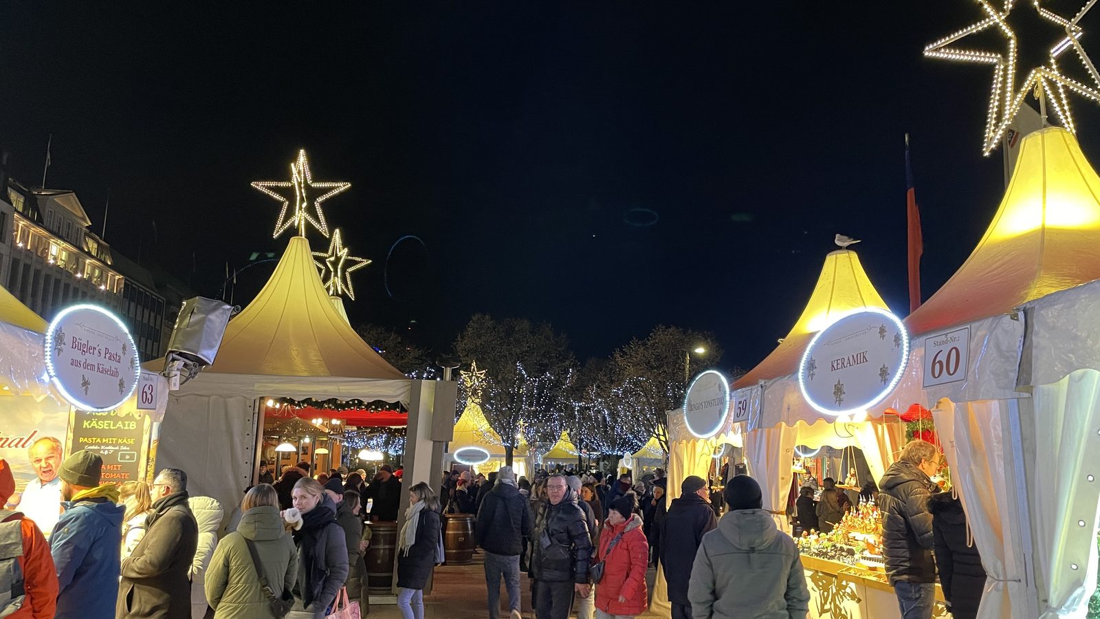 Abendliche Gasse des Weißerzauber mit beleuchteten Sternen, goldenen Zeltdächern und Besuchern zwischen den Ständen