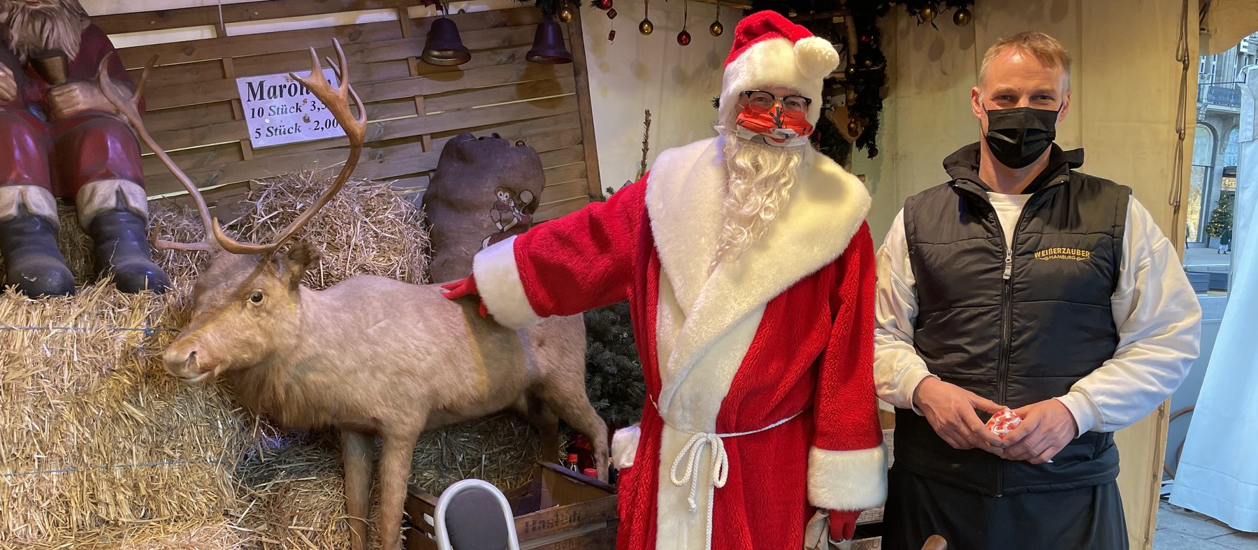 Der Weihnachtsmann mit einem Marktmitarbeiter am Maronistand, mit Rentier-Figur und frischen Maronen